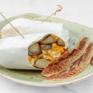 A breakfast plate with a breakfast burrito and crispy bacon strips.