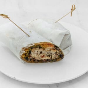 A wrapped burrito with visible filling on a white plate.